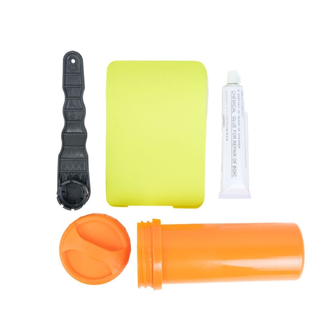 A travel first aid kit set laid out on a white background, including an orange plastic bottle with its cap removed, a bright yellow rectangular item, a black plastic tool, and a white tube of ointment.