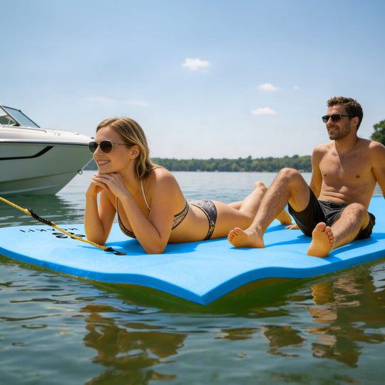 Two people relaxing on a floating platform in the water with a boat in the background.