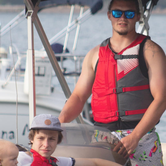 Two people on a boat wearing life vests with a marina background