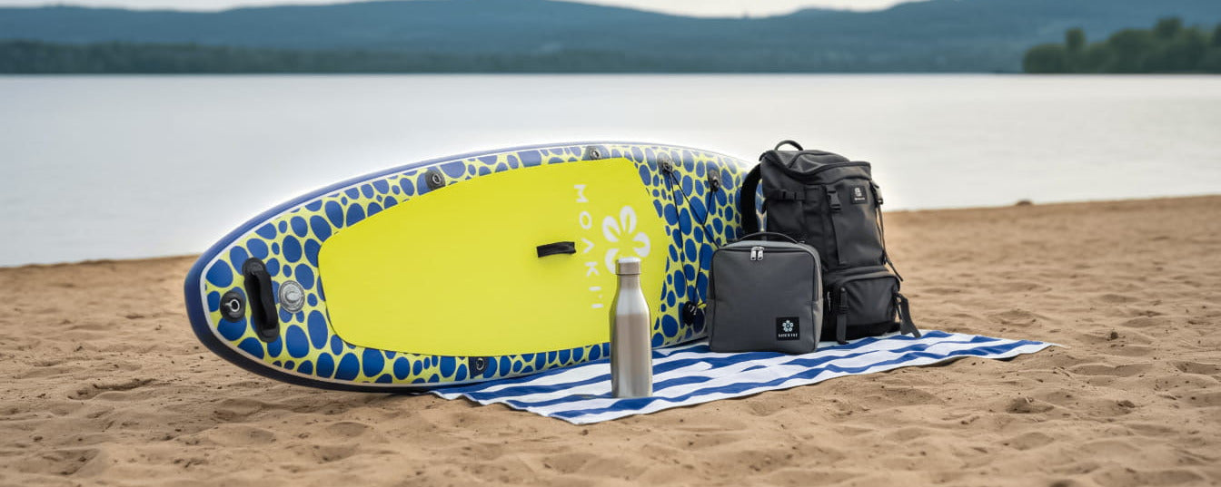 Inflatable paddleboard with backpack and bottle on a towel by a lake