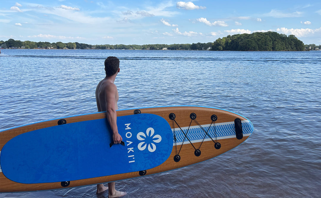 A paddler holding the 11' Kiva by the center handle, demonstrating its easy ~20 lb carry weight.
