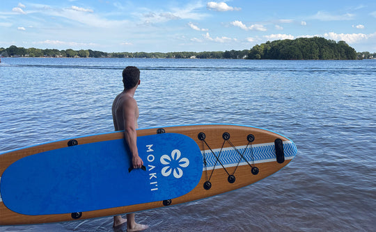 A paddler holding the 11' Kiva by the center handle, demonstrating its easy ~20 lb carry weight.