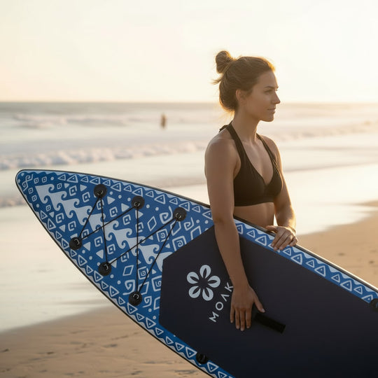 Woman standing on the shore holding the Seeker board, showcasing its manageable carry weight.