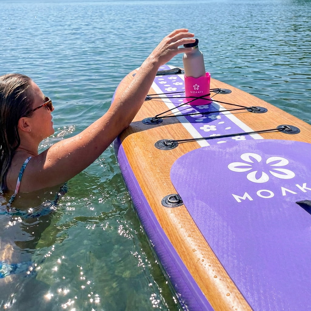 A woman in the water holds a pink bottle resting on a purple and wood paddleboard with the brand name MOLK visible on the board.