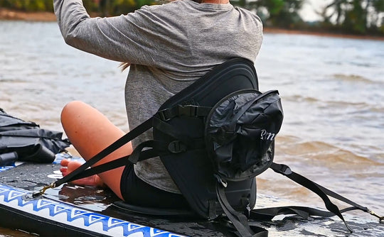 Person sitting on a paddleboard with a kayak seat, water in the background