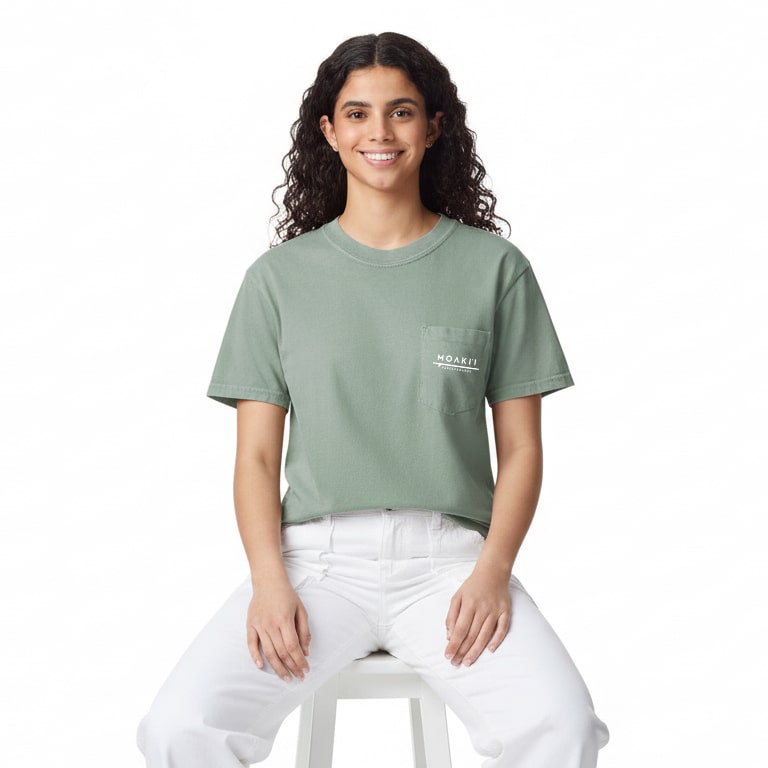 Woman wearing a green t-shirt with a logo, sitting on a white stool against a white background