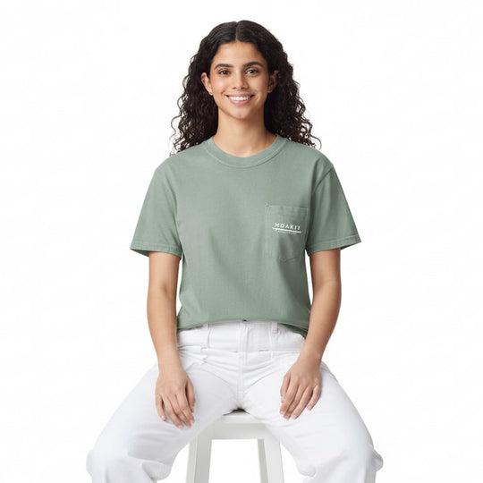 Woman wearing a green t-shirt with a logo, sitting on a white stool against a white background