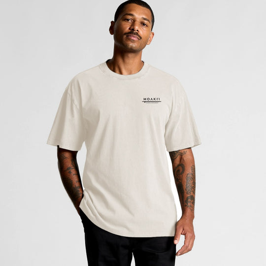 Man wearing a beige t-shirt with a logo on a plain background