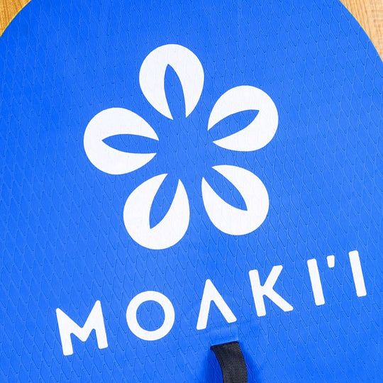 Detailed view of the Moaki'i signature flower logo on the blue non-slip deck pad.