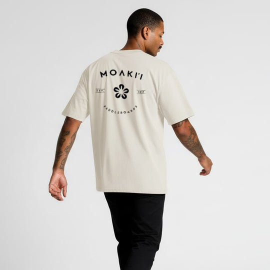 Man wearing a beige t-shirt with 'MOAKI'I' logo on the back against a white background