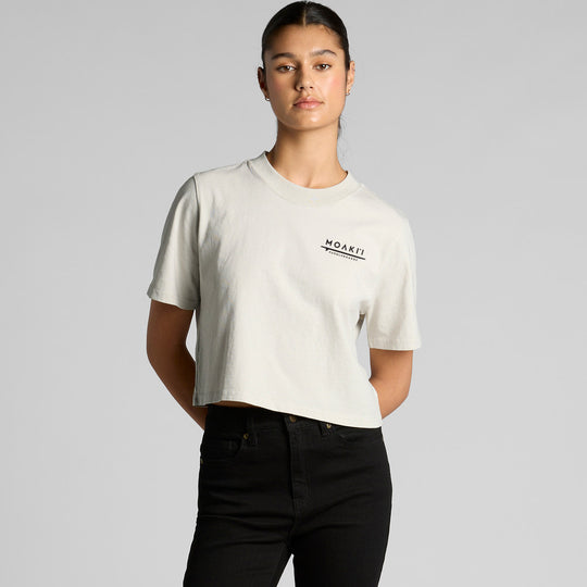 a teenage girl wearing a white cropped t-shirt with a moaki'i logo on a gray background