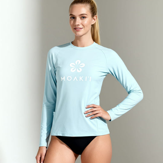 Woman wearing a light blue long-sleeve shirt with a logo on a gray background