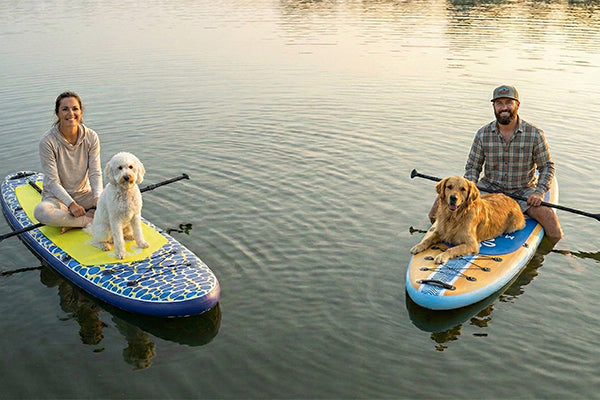 Two paddlers with their dogs on Moaki'i Trekker boards, showing its pet-friendly stability for calm water.