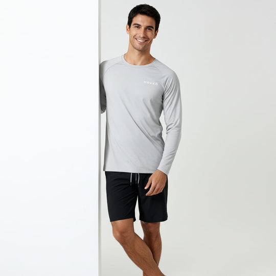 Man wearing a gray long-sleeve rash guard and black shorts on a white background