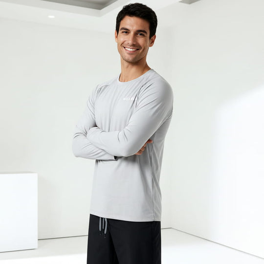 Man wearing a gray long-sleeve water shirt and black swim trunks standing against a white background