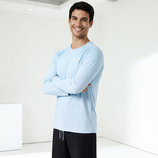 Man wearing a light blue long-sleeve shirt and black pants standing against a white background
