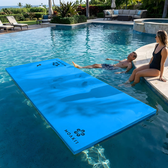Blue floating mat with 'Moakii' branding in a pool, with two people nearby.