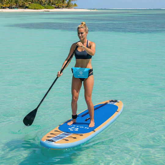 Woman paddleboarding on a clear blue ocean with a tropical island in the background