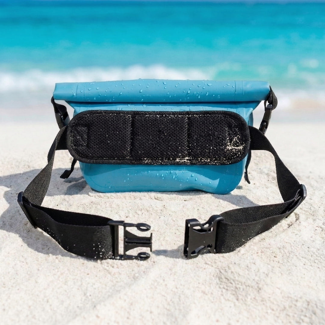 Blue waterproof bag with black strap on a sandy beach with ocean in the background