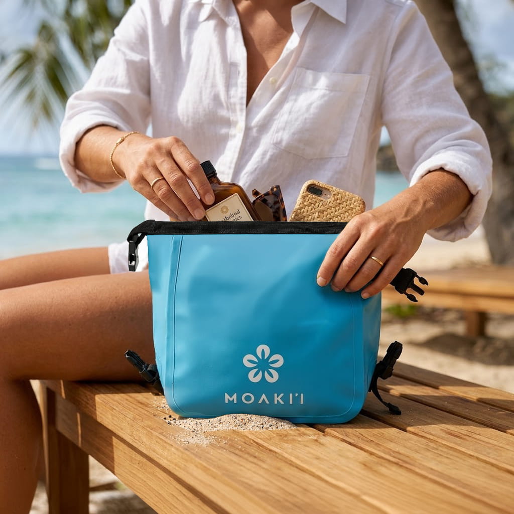 Person organizing items into a blue Moakii pouch on a beach.