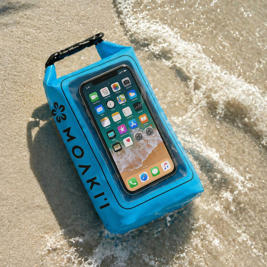 Blue Moakii phone case with a smartphone inside, on sand with water.