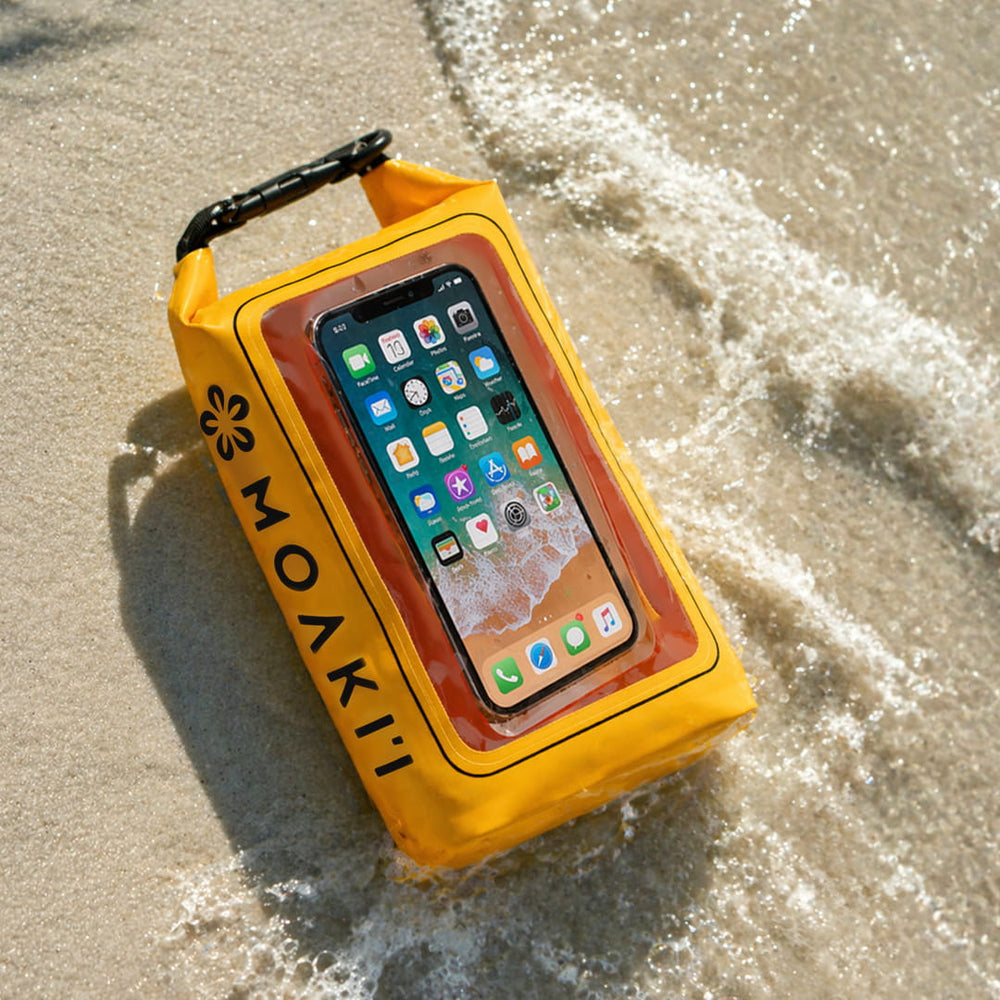 Yellow Moakii waterproof phone case with a smartphone inside, on a sandy beach with waves.