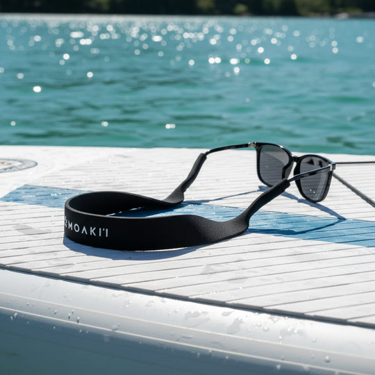 Black sunglasses with a strap on a dock by a body of water