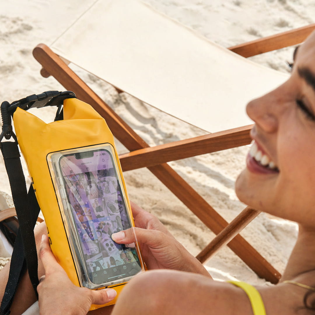 Person using a phone in a yellow waterproof case on a beach